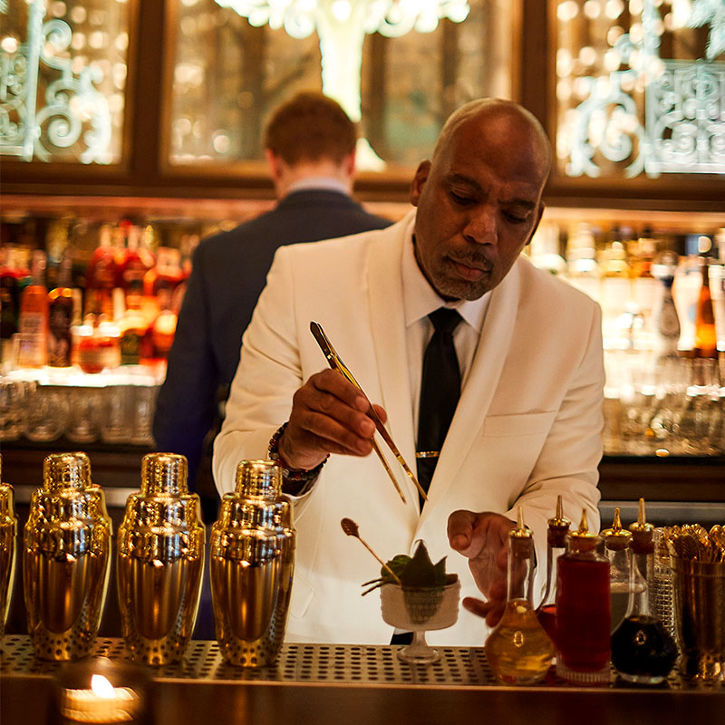 Café Carmellini bartender in white jacket using tongs and making a cocktail